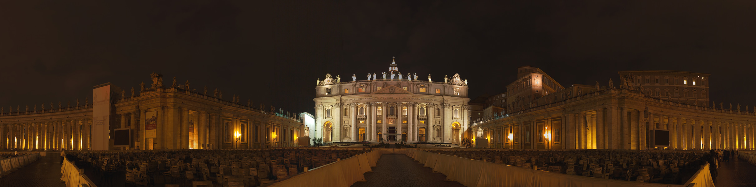 Grand illuminated cathedral facade with colonnaded plaza, night scene, warm gold and white lighting against dark sky