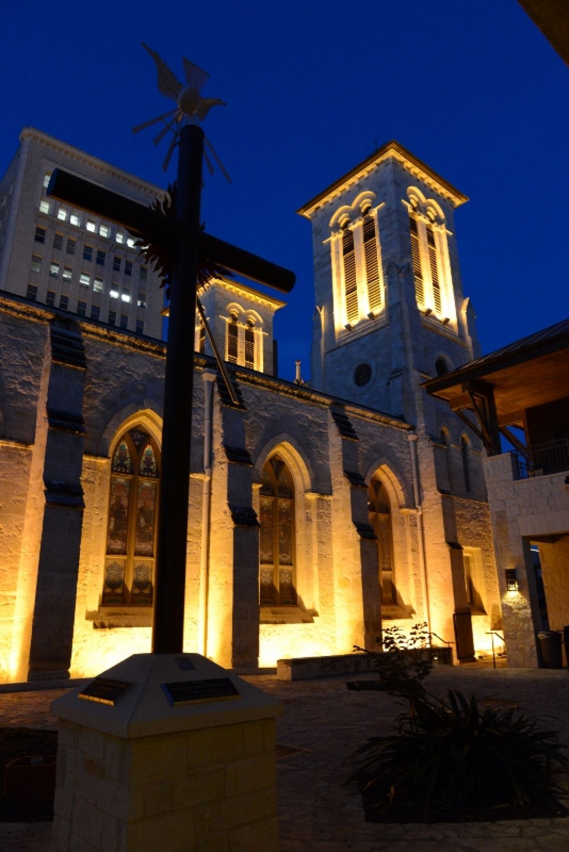 Nighttime exterior view of a stone church with illuminated twin towers and stained glass windows, deep blue sky, warm golden light