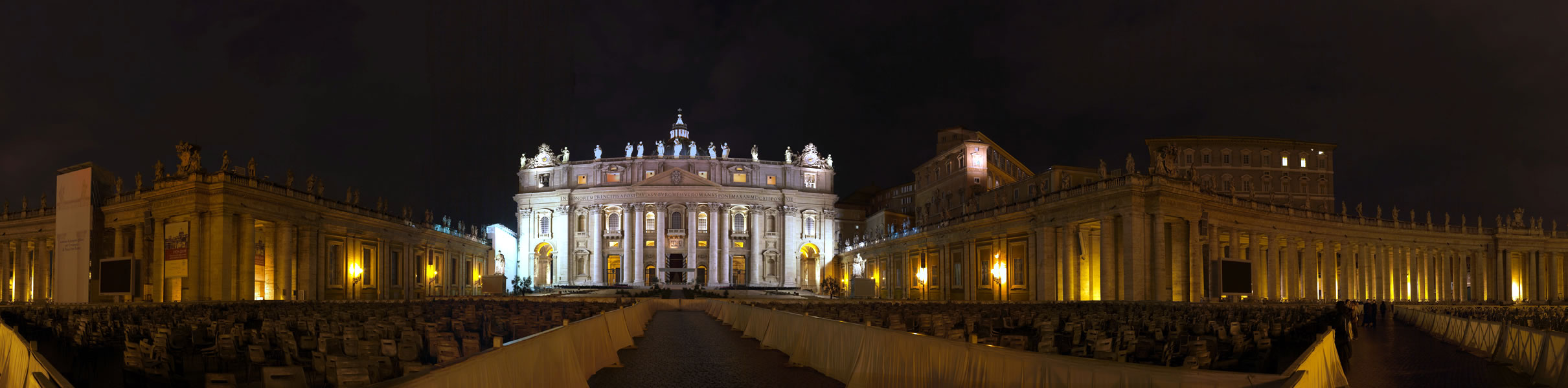 Grand illuminated cathedral facade with colonnaded plaza, night scene, warm gold and white lighting against dark sky